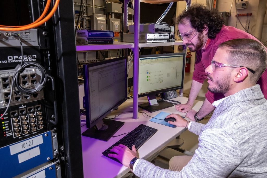Two technicians working at a computer beside a network rack